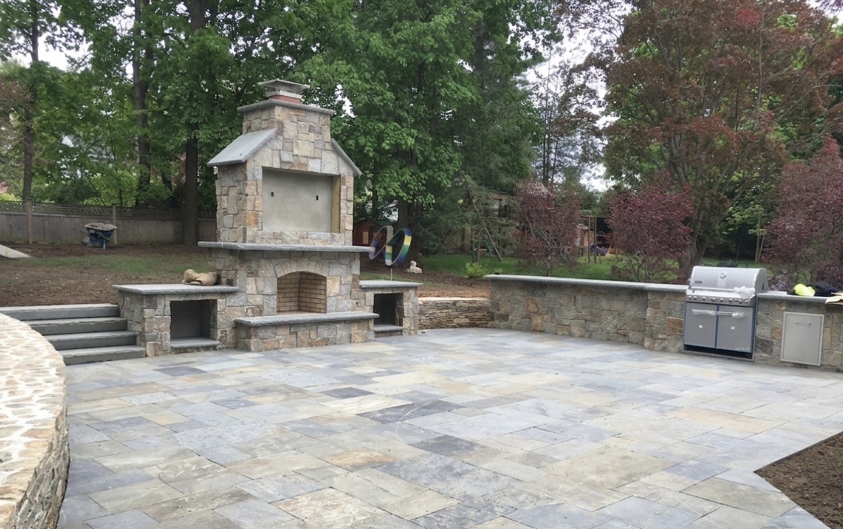 Large paver patio with custom stone fireplace, stone seating wall and outdoor grill station